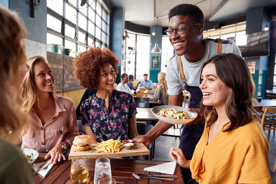 Group of friends interacting with waiter at restaurant